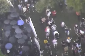 As riot squad prepare weapons under umbrellas at left - a weapons cart is wheeled in by 'peaceful protest' mob at right